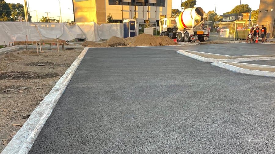 Freshly poured permeable concrete car park edged in protective plastic, with the concrete truck and crew at the far end