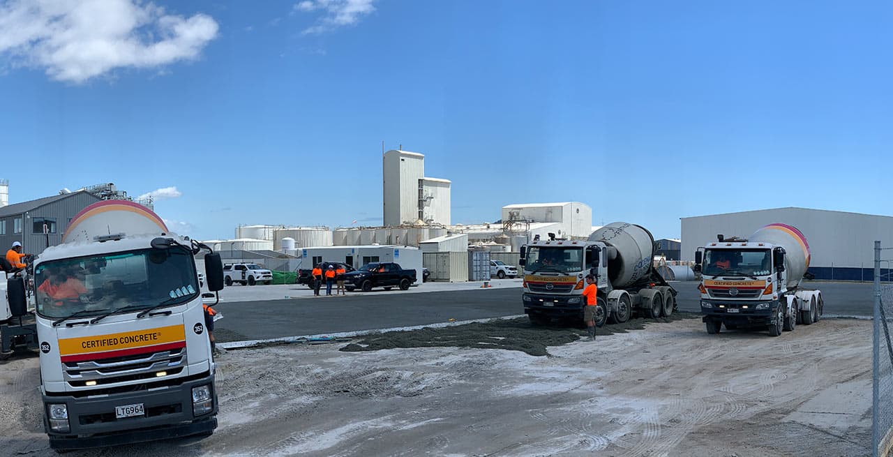 Three concrete trucks lined up beside a newly placed permeable concrete slab at an industrial site