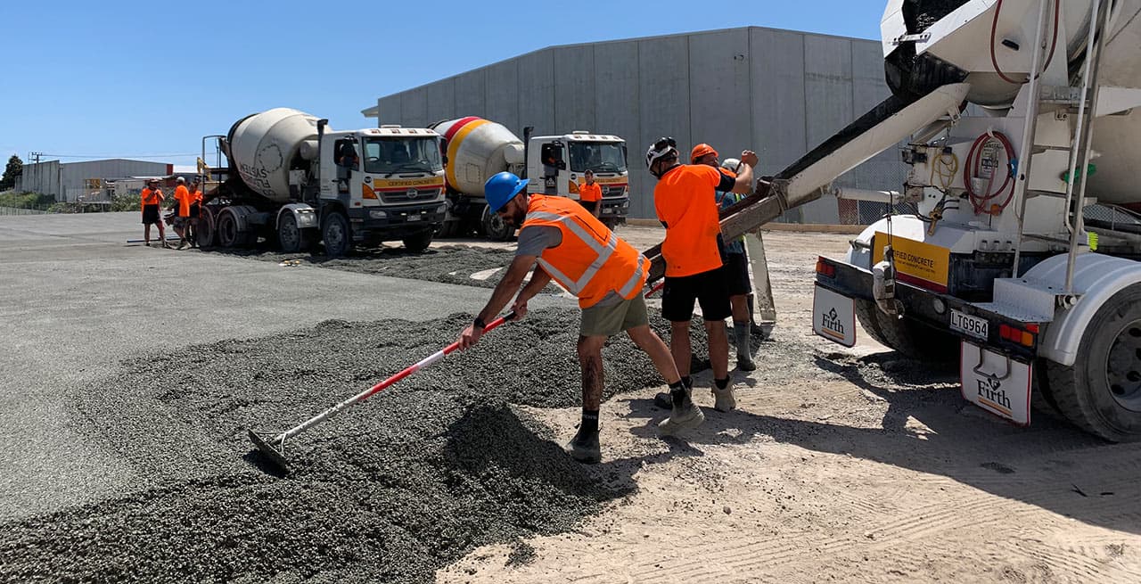 Crew raking permeable concrete off a truck chute across a large industrial hardstand