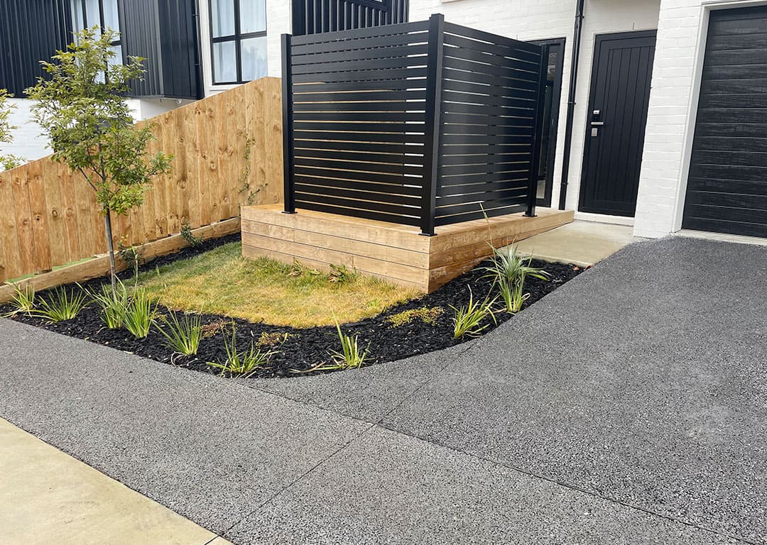 Charcoal permeable concrete driveway meeting the footpath crossover beside a small lawn and garden bed at a new townhouse