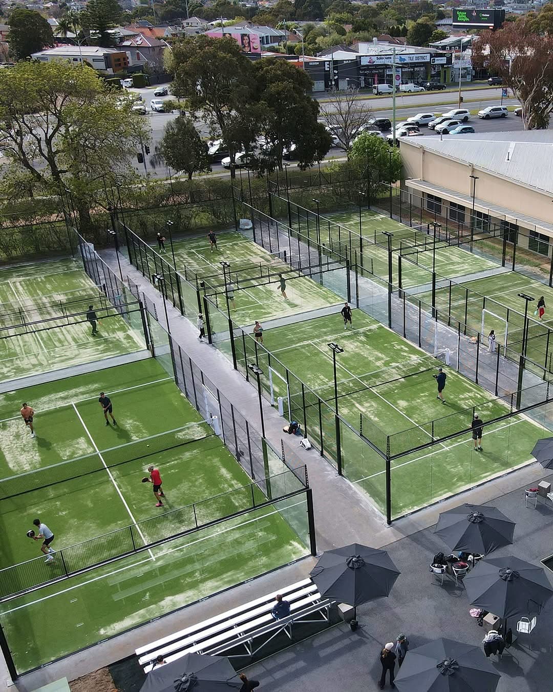 Aerial view of padel courts in play, with walkways between the turf courts and umbrellas over a seating area